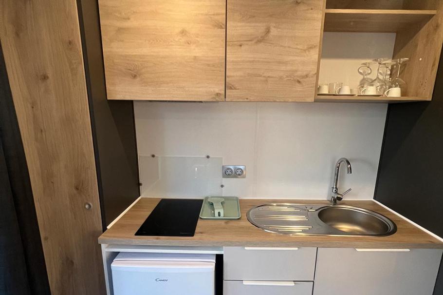 Piccola cucina moderna con frigorifero, piano cottura, lavello e armadietti in legno chiaro.
