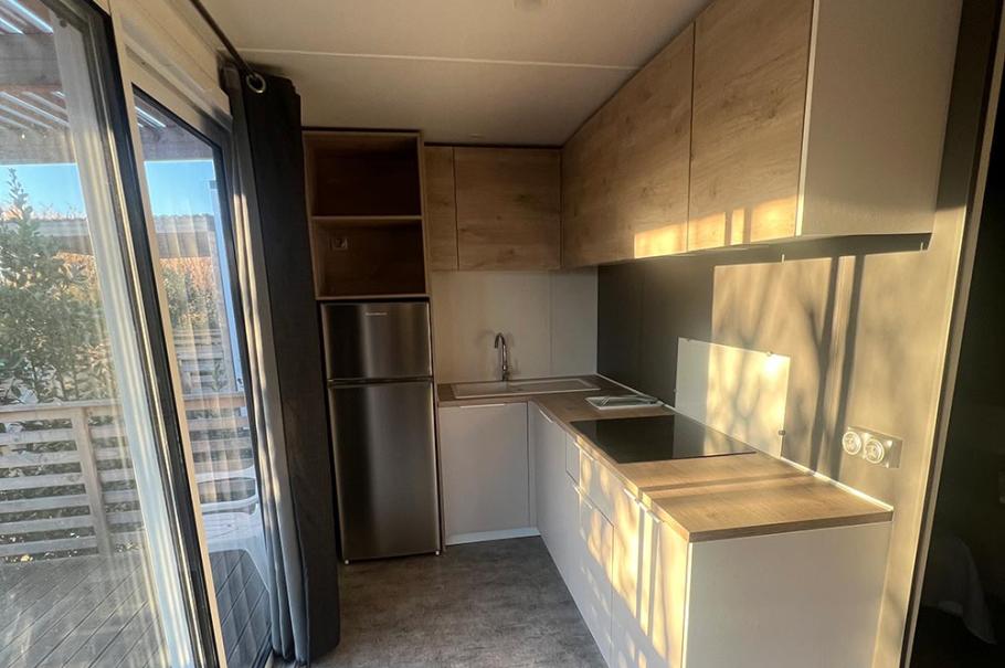 Cucina moderna e compatta con elettrodomestici, armadietti in legno chiaro e pavimento grigio.