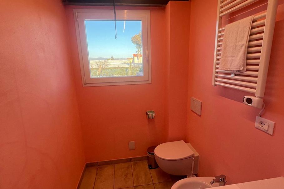 Bagno moderno con pareti rosa, finestra, bidet, WC e scaldasalviette.
