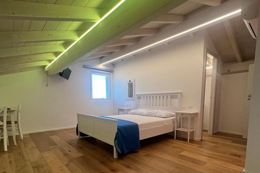 Camera moderna con letto, parquet e luci a LED sul soffitto inclinato.